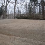 A freshly leveled gravel surface in a wooded area, ideal for building a pole barn, with bare trees in the background on a cloudy day. Kentucky Builders And Excavating