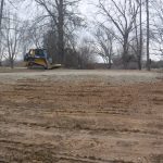 A small bulldozer is excavating and leveling gravel for a pole barn on a muddy construction site, surrounded by leafless trees on an overcast day. Kentucky Builders And Excavating