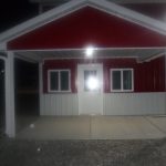 A red and white pole barn at night with a covered entrance, two square windows, and a door. The flash from the camera creates a bright glare on the door’s window while the surrounding area remains dimly lit. Kentucky Builders And Excavating