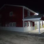 A red and white metal pole barn building with a covered entrance and multiple garage doors is illuminated at night by exterior lights. The surrounding area appears to be gravel. Kentucky Builders And Excavating