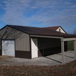 A metal pole barn with a white garage door, a white side door, and a covered carport area. The building sits on a concrete slab surrounded by grass, leaves, and a partly cloudy sky—ideal for storage or workshop use. Kentucky Builders And Excavating