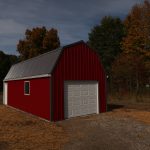 A red pole barn-style shed with a gray metal roof and white garage door stands on a plot of land with straw and gravel, surrounded by trees with autumn foliage under a partly cloudy sky—an ideal building after recent excavating. Kentucky Builders And Excavating