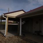 A partially enclosed pole barn carport with a gravel driveway, adjacent to a house with white columns and a red metal roof, under a partly cloudy sky. Kentucky Builders And Excavating