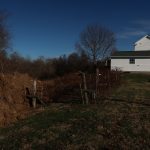 A white house with a green roof stands near a large pile of dirt and a deep trench from recent excavating, next to a grassy yard with leafless trees and a clear blue sky in the background. Kentucky Builders And Excavating