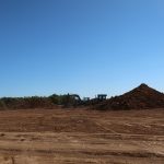A construction site with two excavators excavating near several piles of dirt under a clear blue sky, surrounded by trees in the background, preparing the ground for a new building. Kentucky Builders And Excavating
