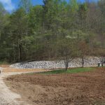 A dirt road winds through a building site with a bulldozer near a gravel pile. Trees with green foliage line the background, and the sky is partly cloudy—perfect for excavating work. Kentucky Builders And Excavating
