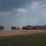 A large pole barn sits on a gently sloping hill under a cloudy sky, with a mix of dry, brown grass and green grass in the foreground and signs of recent excavating near the trees along the horizon. Kentucky Builders And Excavating