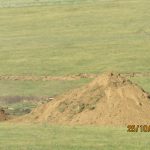 A yellow bulldozer is parked beside a large pile of dirt on a grassy field, likely excavating for a pole barn or building project. Tire tracks and a dirt path are visible, with the date and time 25/10/2023 01:52 at the bottom right. Kentucky Builders And Excavating