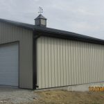 A detached, light gray metal pole barn garage with a white door and black roof stands on a gravel driveway. A cupola with a weather vane tops the roof. The date and time 13/06/2024 19:24 are displayed in the corner. Kentucky Builders And Excavating