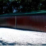 A large brown metal pole barn with a green roof stands on a gravel surface, surrounded by trees in the background. Kentucky Builders And Excavating