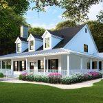 White farmhouse style home featuring a full wrap around porch with traditional wooden railings, rocking chairs, and columns extending across the front and side elevations